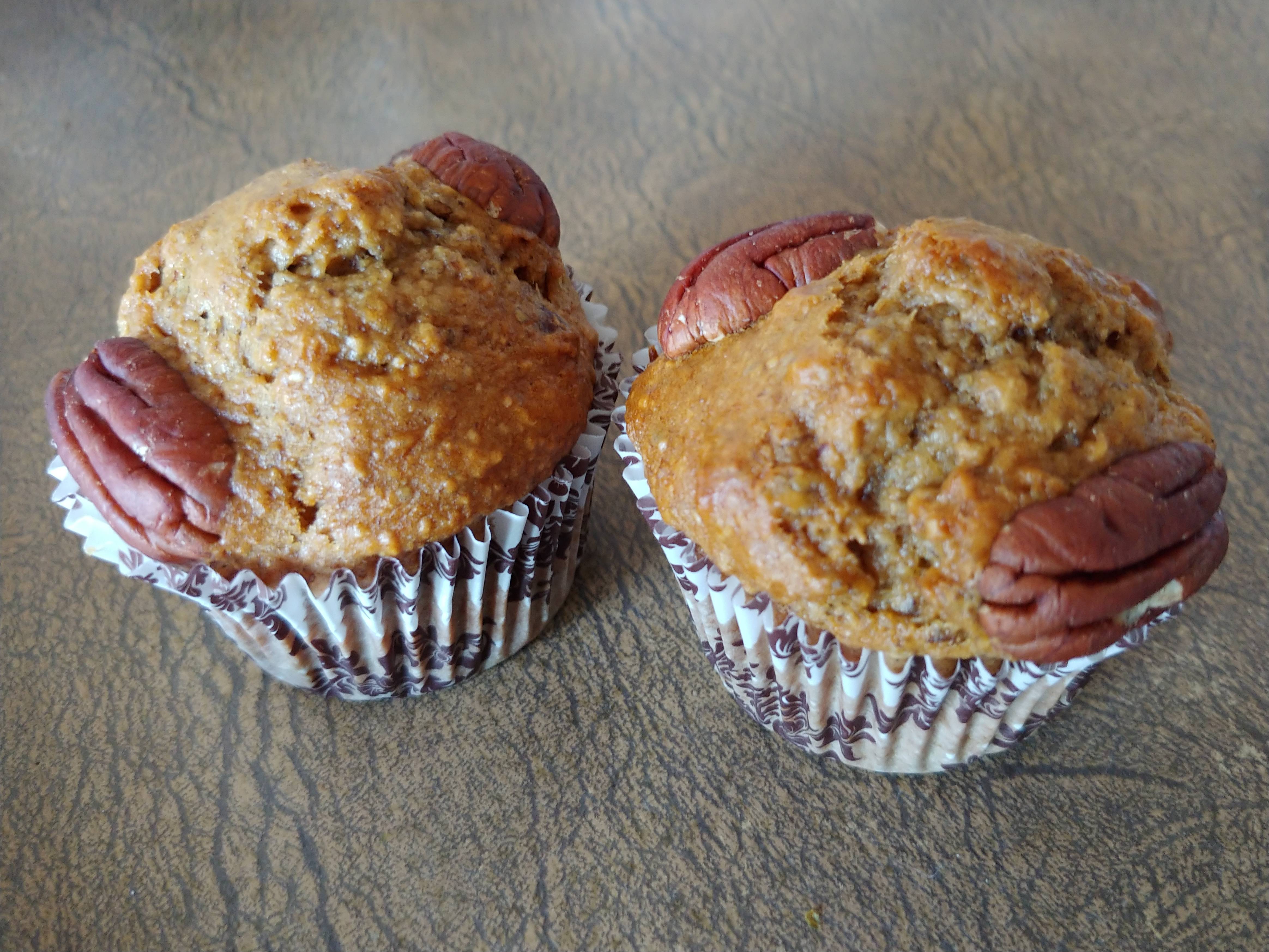 Two Banana Bread Muffins on an old brown kitchen bench. Pecans in the top kind of look like alien eyes